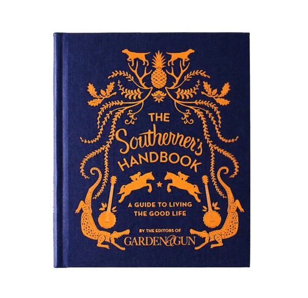 Hardcover book titled The Southerner's Handbook: A Guide to Living the Good Life with orange decorative illustrations on a navy blue cover, offered by Knotty and Board, an independent retail for decor and gifts.
