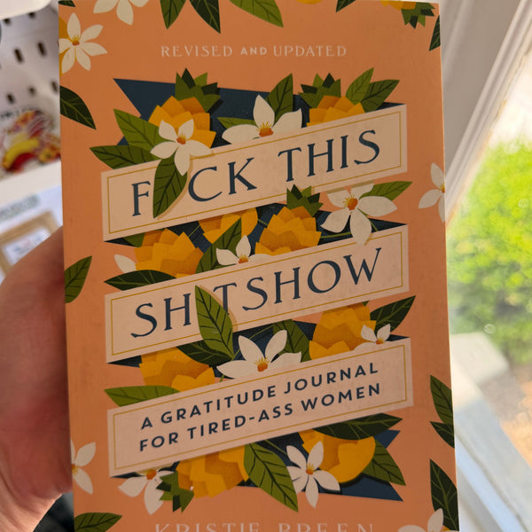 Hand holding a colorful gratitude journal titled F*ck This Sh*tshow with floral design, featuring a humorous and relatable theme for tired women, perfect for gifts or decor.