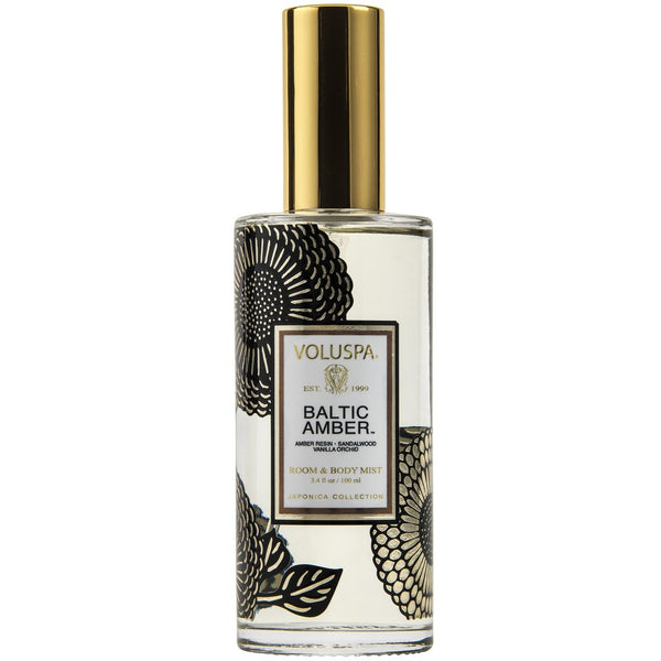 Voluspa Baltic Amber Room & Body Spray in a clear glass bottle with black floral designs and a shiny gold cap, perfect for adding elegant decor and fresh scents.