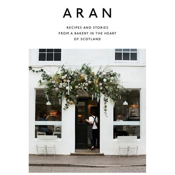Cover of Aran: Recipes and Stories from a Bakery in the Heart of Scotland - Flora Shedden featuring a charming bakery entrance adorned with lush floral decor, reflecting Knotty and Board’s curated gifts and kitchen ambiance.