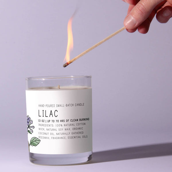 Hand lighting the Just Bee Lilac Candle, 13 oz, a hand-poured soy wax candle with natural cotton wick and lilac floral design, perfect for decor and gifts from Knotty and Board.