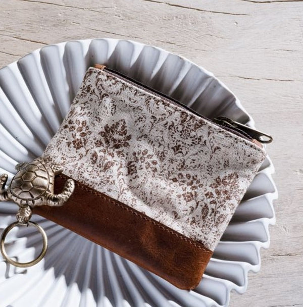 Brown Floral Canvas Zip Pouch 10" featuring a delicate floral pattern on canvas with a brown leather bottom, styled on a decorative white plate, ideal for gifts and decor.