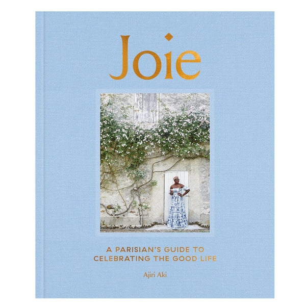 Joie book with a blue cover featuring a photo of a woman in a floral dress standing by a flower-covered stone wall, celebrating Parisian lifestyle and decor themes.