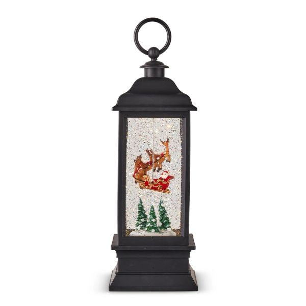 Lighted Water Lantern with Animated Santa Flying, 11 in. features a classic black lantern frame with illuminated scene of Santa in his sleigh flying above snow and pine trees, perfect decor or gifts from Knotty and Board. Every Room Needs A Little Knotty and Board.
