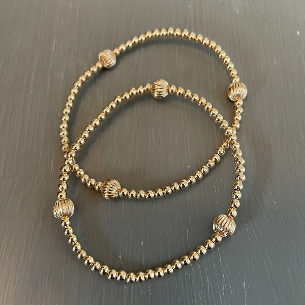 Morgan & Me 4mm 14k Gold Filled Bracelet with 14k Gold or Sterling Silver Bead displayed on a dark surface, showcasing delicate gold beads with textured accent beads, a perfect jewelry gift from Knotty and Board.