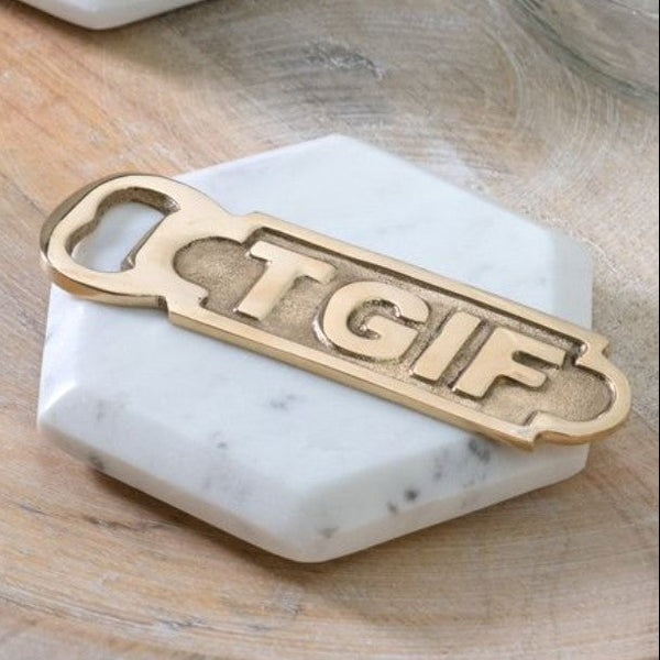 Brass TGIF Bottle Opener resting on a white marble hexagonal coaster on a wooden surface, perfect for kitchen or entertaining decor.