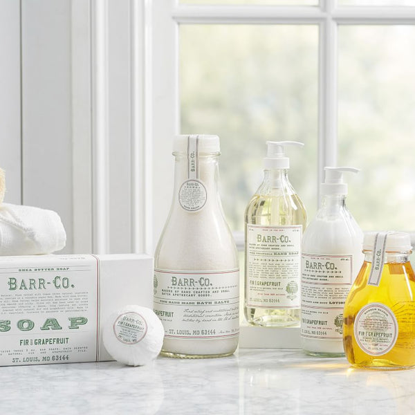 Collection of Barr & Co. Fir & Grapefruit Dish Soap and matching bath products displayed on marble countertop near window, styled with white towels for kitchen decor.