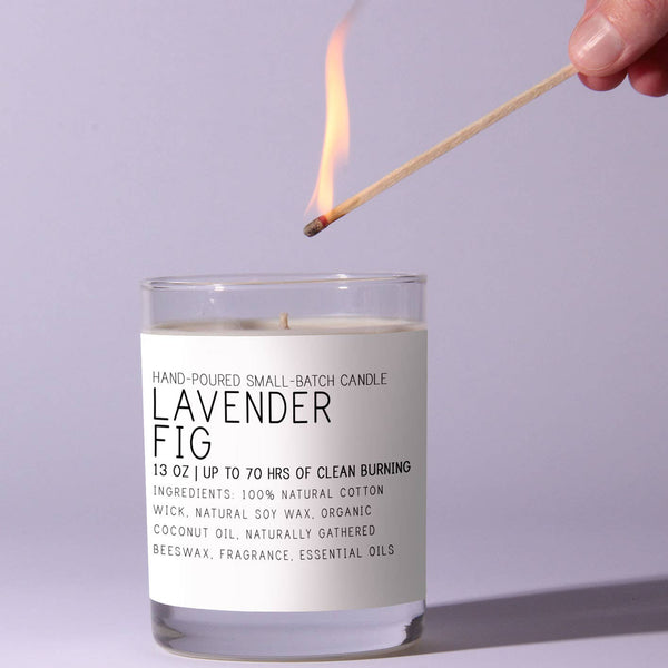 Hand lighting a Just Bee Lavender Fig Candle, 13 oz, featuring natural soy wax and essential oils, perfect for home decor and gifts from Knotty and Board.